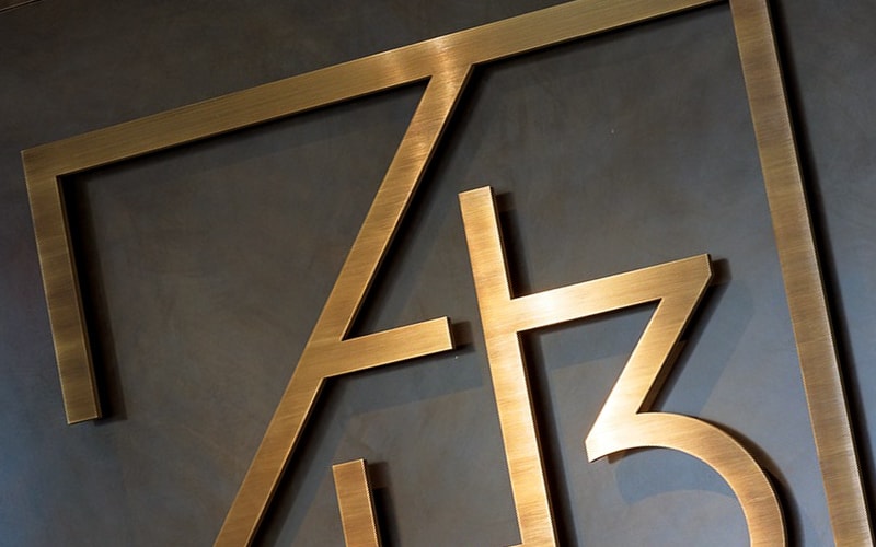 oxidized oil rubbed brass logo mounted with standoffs on metal wall office lobby closeup detail