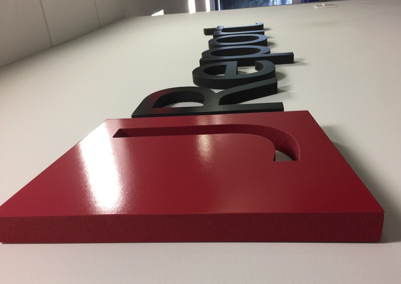 Side view of foam sign with red logo and black letters on white wall