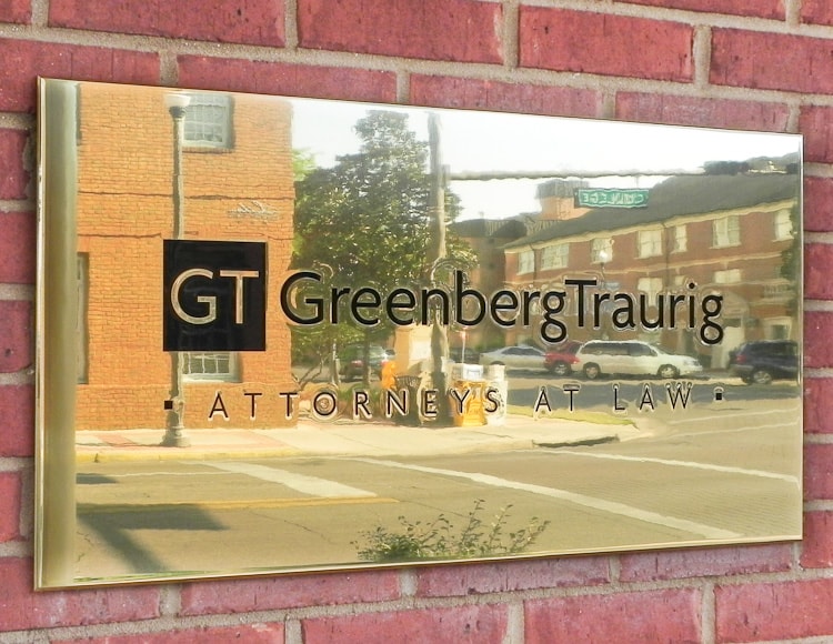 a shiny polished brass plaque with black text mounted outside on brick wall building 